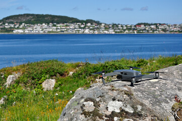Drone standing on a rock against the background of grass. In the back plan the sea, mountains and the city.