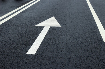 Arrow sign on the road. White arrow on the asphalt. White forward arrow on a blurry street...