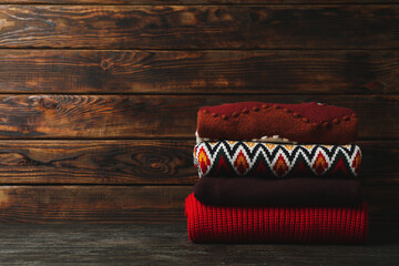 Pile of sweaters on wooden background, space for text