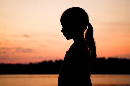 Silhouette of a little girl standing near a lake at sunset