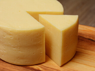 Cut a piece of cheese triangular shape from a large cheese head. On a wooden surface, close-up