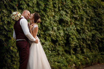 Romantic couple newlyweds, bride and groom stands and holding bouquet of flowers and greens, greenery in the Botanical green garden. Wedding ceremony on nature.