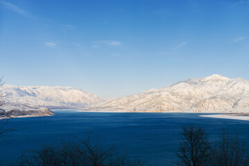 Fototapeta na wymiar Charvak reservoir with blue water on a clear winter day in Uzbekistan, surrounded by snow-capped mountain peaks of Tien Shan