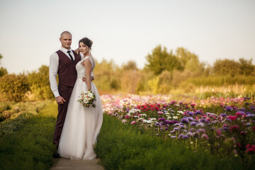 Walking the bride and groom in a beautiful flower garden. Portrait of a happy wedding couple on their wedding day,beautifully dressed newlyweds tenderly hug while walking in a park