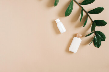 The concept of pure beauty and organic cosmetics for body care. Bottles of white cream lie on a beige background and a branch of a tropical plant. Copy space