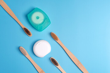 Dental floss containers and bamboo toothbrushes on blue background. Daily oral hygiene, teeth care and health. Cleaning products for mouth. Dental care concept. Empty place for text or logo