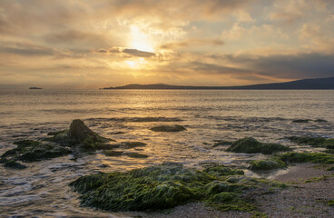 Obraz premium Foaming wave, breaking at sunrise with a rocky shoreline