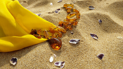 Fototapeta na wymiar Amber luxury jewelry necklace and raw piece of natural Baltic amber with yellow silk scarf on the sand. 