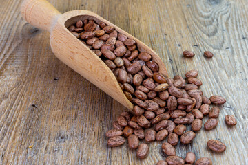 dried beans spilling from wooden spoon, on wooden table