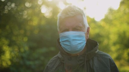 Senior man wearing anti virus mask is walking in the nature.