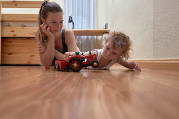 Fototapeta premium Mom and her toddler son plays with red car in their cosy room
