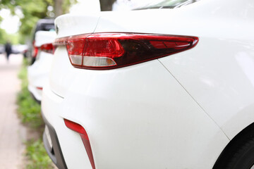 Rear red headlight of white car close up. There are many car in parking lot.