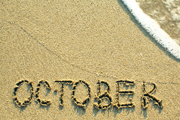 October inscription on the sand beach with the soft wave.