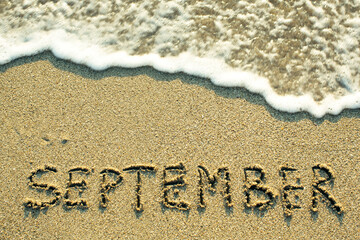 September inscription on the sand beach with the soft wave.