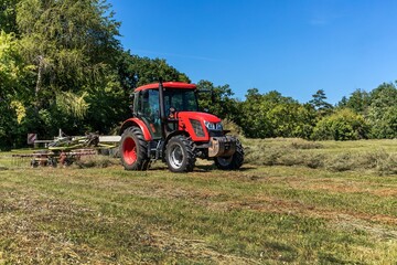 Red tractor working in a field with a two-rotor tedder. Drying hay in the meadow. Work on an agricultural farm.