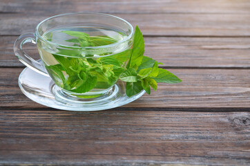 Freshly made hot aromatic mint tea in a glass cup and fresh leaves on a wooden table close-up....
