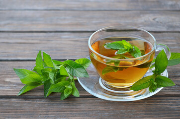 Cup of freshly made hot mint tea with fresh green mint leaves on a old wooden table. Concept of a...
