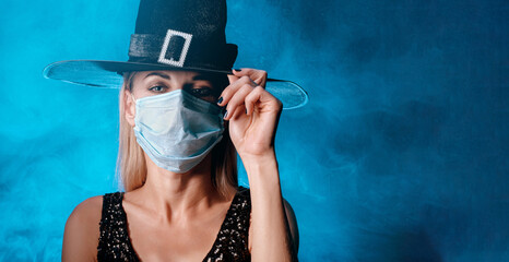 halloween witch in a black hat and black dress with a medical mask on her face. halloween concept 2020