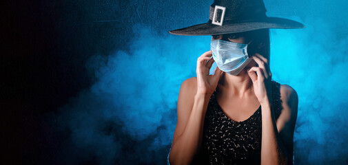 halloween witch in a black hat and black dress with a medical mask on her face. halloween concept 2020