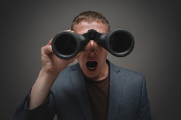 Shocked man is looking through a binoculars close up.