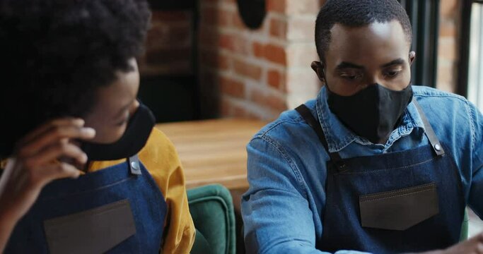 Close up of African American couple in masks doing business calculations and checking bills. Calculating spends and damages. Reopen after quarantine. Counting at laptop computer Small entrepreneurship