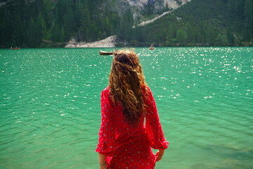 Girl with brown wavy hairs moved by the wind in red dress watching the emeral water of Lago di...