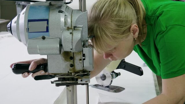 An female worker dressed in uniform cutting a piece of cloth for the production of a sofa in a furniture factory. 4K