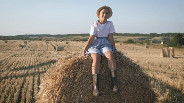 Pretty girl in blue dress walks in a field with haystacks.