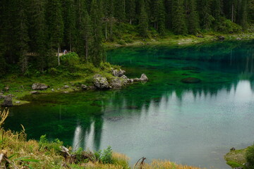 Old couple watching the emerald clear water with pine forest reflection of Lago di Carezza, Sudtirol, Trentino Alto Adige, Dolomites, Italy