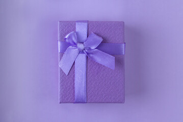 Purple surprise gift with a ribbon on a purple background. A minimalistic concept in mono color. Black Friday, Sales, Giving Gift for Christmas and New Year. Close up. Secret lavender box.