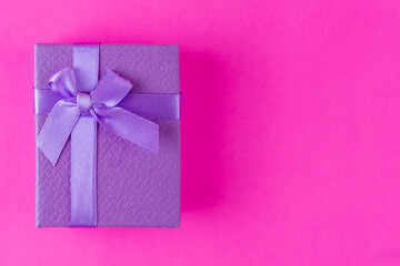 Purple surprise gift with a ribbon on a bright pink background. A minimalistic concept free space for text. Black Friday, Sales, Giving Gift for Christmas and New Year. Secret lavender box. Top view