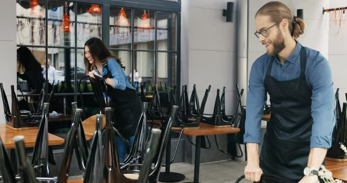 Caucasian couple of baristas, male and female in masks and gloves cleaning desks and chairs in bar. Waiter and waitress clean and preparing public place in cafe. Reopen concept. Preparation.