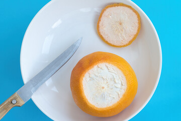 Orange grapefruit with cut off the top end, knife on white plate on blue background. Top view, diet concept