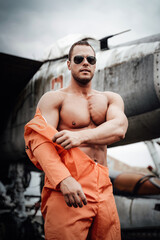 Fototapeta na wymiar American serious guy posing near stationary old aircraft in abandoned place. Crashed airplanes in the war airport and military technician.