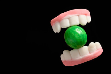 Halloween treats, gummy teeth biting a watermelon gum, on black background