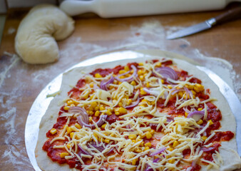 Pizza angerichtet roh auf einem Backblech mit Käse bestreut, Mehliges Brett, zubereitung