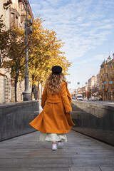 Street style clothing. Teenager girl in a coat, sneakers and a light skirt walks in the city