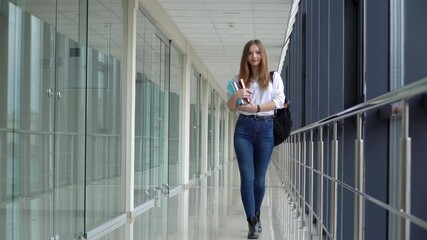 Female student with a book walking in the university. Exam preparation. New modern fully functional education facility
