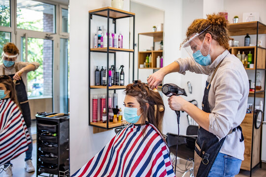 Working during covid-19 or coronavirus concept. Hairstylist drying the hair of a client in a beauty center. Woman in protective medical mask and hairdresser. Hairdressing salon opened! 