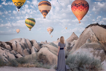 The girl watches as the balloons fly over the rocks in the morning at dawn. Turkey