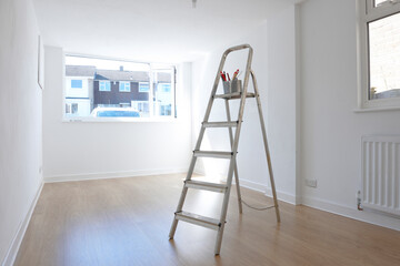 ladder with paint pot and brushes standing in empty room