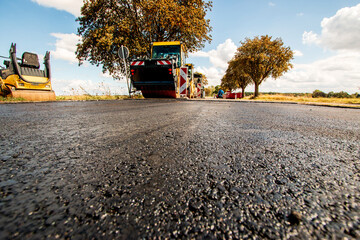 Tiefer Blick über eine frisch asphaltierte Strassendecke auf Baumaschinen