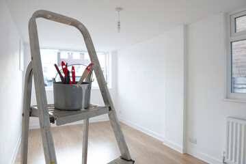 ladder with paint pot and brushes standing in empty room