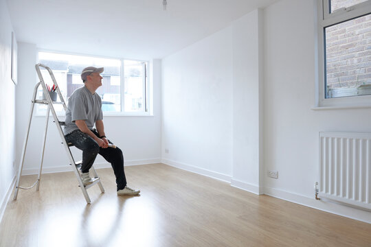man sitting on ladder looking at newly decorated white painted room