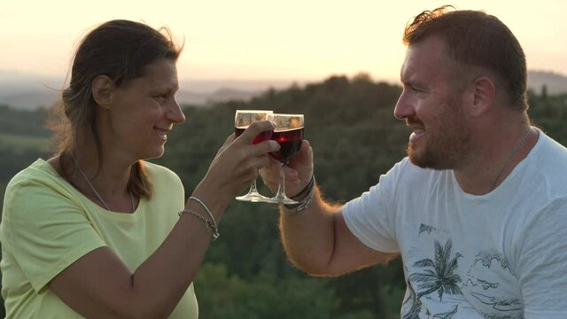 young couple takes an aperitif drinking a glass of red wine at sunset exchanging cuddles
