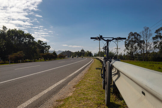 Front Shot to a black Mountain Bike clining to a safety highway metal fence in a sunny day. Travel andbicycle concept