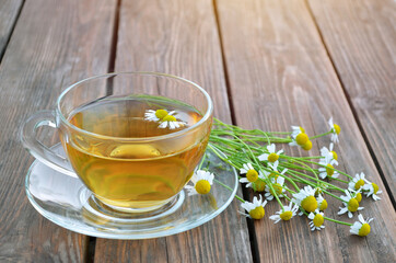 Freshly made hot chamomile tea in a glass cup on a wooden table close-up. Healthy tea concept.