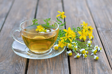 Cup of hot herbal tea from St John's wort and Matricaria chamomilla on a wooden table close-up. Concept of a healthy lifestyle.