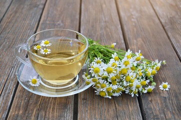 Bouquet of Matricaria chamomilla and cup of chamomile tea on a wooden table close-up. Concept of a healthy lifestyle.