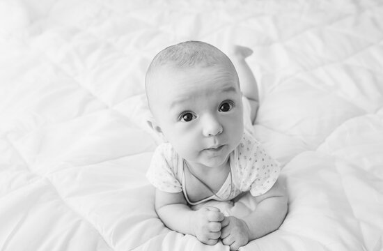 A small, newly born, smiling child, a boy, lies on a white bed and tries to crawl. 3, 4 months from the moment of birth. Photography, concept.